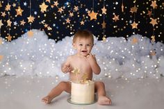 a baby sitting on the floor in front of a cake with stars hanging from it