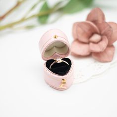 an open pink ring box sitting on top of a white table next to a flower