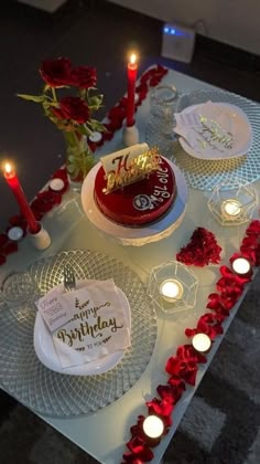 a table topped with two cakes covered in frosting and red roses next to candles