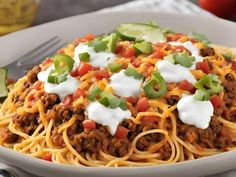 a white bowl filled with spaghetti topped with chili and sour cream sauce, avocado wedges on the side