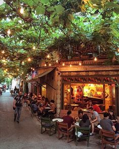 many people are sitting at tables outside under the trees and hanging from the ceiling with lights