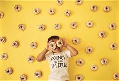 a man holding two doughnuts over his eyes in front of donuts on a yellow background