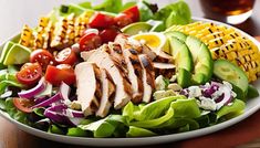 a salad with chicken, lettuce, tomatoes, corn on the cob and avocado