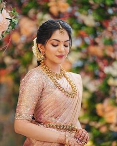 a woman in a pink sari and gold jewelry standing next to a flower bush