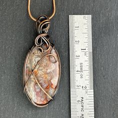 a wire wrapped pendant sitting next to a ruler