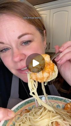 a woman is eating spaghetti with shrimp on it