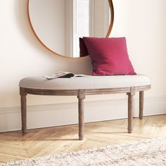 a white bench with a pink pillow and a round mirror on the wall behind it