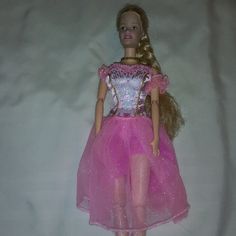 a barbie doll wearing a pink dress and shoes on a white sheeted bed spread