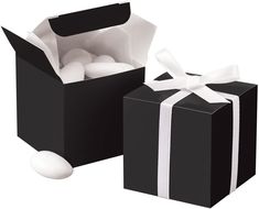 two black boxes with white ribbon and one has a gift box in the middle that is filled with balls