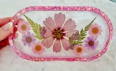 a hand holding a pink and white tray with flowers painted on it