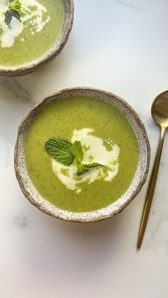 two bowls filled with green soup on top of a white counter next to a spoon