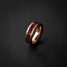 a wedding band with red glitter inlaying the center on a black surface,