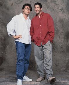 two men standing next to each other in front of a cement wall with their hands on their hips