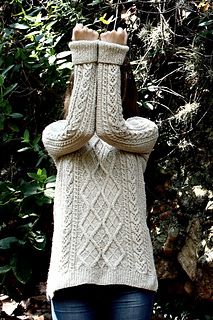 a woman standing in front of some trees with her hands up to her face while wearing a sweater