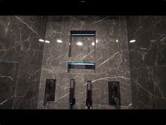 a bathroom with grey marble walls and blue trim around the shower head, along with three black hairdryers