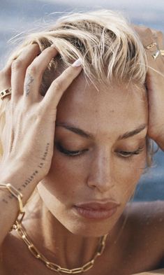 a woman holding her hands to her head while sitting next to the ocean with tattoos on her arms