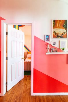 an open door leading to a bedroom with pink and red walls, wooden floors and pictures on the wall