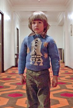 a young boy standing in a hallway wearing a sweater with words on it and stars