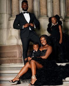 a man in a tuxedo poses with two women and a child on the steps