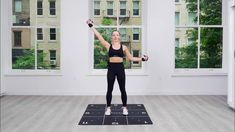 a woman standing on a yoga mat with her arms in the air and holding two dumbbells