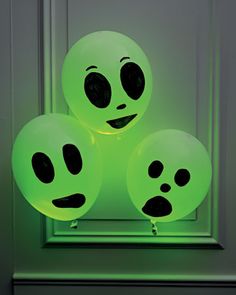 three glow balls with faces on them sitting in front of a window, one is green and the other is black