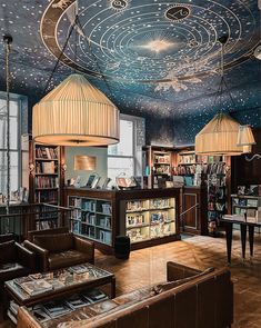 a library with many books on shelves and lamps hanging from the ceiling over it's seating area