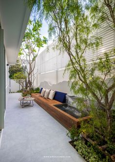 an outdoor seating area with trees and plants on the side of the house, along with a bench