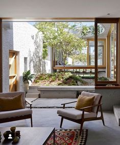 an open living room with two chairs and a table in front of large windows that look out onto the backyard