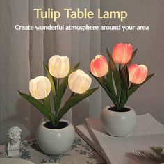 two white vases filled with pink flowers on top of a table next to an open book