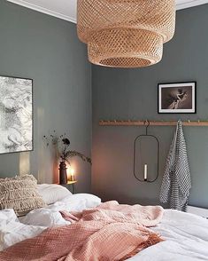 an unmade bed in a bedroom with a wicker light fixture hanging above it