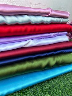 a stack of different colored fabrics sitting on top of green grass next to a wall