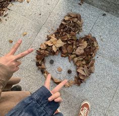 two people sitting on the ground with their hands up in front of a pile of leaves