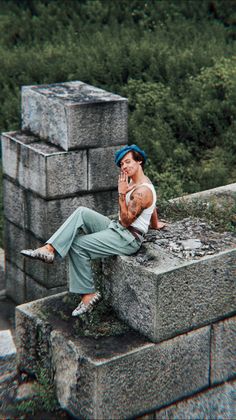 a man sitting on top of a stone wall talking on a cell phone while holding his hand up to his face