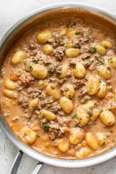 a pot filled with stew and potatoes on top of a white countertop next to silver spoons