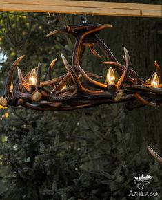 a deer antler chandelier hanging from a wooden beam in front of trees