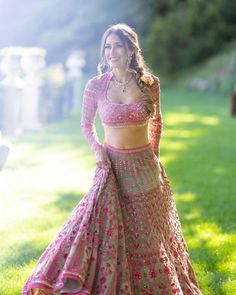 a woman in a pink and gold lehenga standing on the grass with her arms behind her back