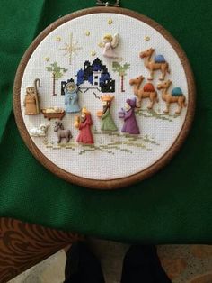 a cross stitch christmas scene with the birth of jesus on it and other decorations hanging from a hoop