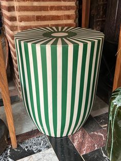 a large green and white striped stool sitting on top of a tiled floor next to a brick wall