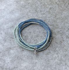 This beautiful long stretch wrap bracelet is hand beaded with a stunning color block mix of high quality delicate 2mm Miyuki, Toho and Czech glass seed beads accented with a tiny silver plated flower and leaf pendant. In beautiful summery blues and greens mixed with shiny sterling silver accents, the cord is secured with professional jewelry adhesive. Bracelet is 44" in length and wraps 6 times on an average 7" wrist size, Looks beautiful alone or stack several together! Can also be layered as a necklace wrapped 2-3 times or even an anklet! Each are totally unique and accent bead varies with each design. Blue Beaded Bracelets With Tiny Beads For Everyday, Everyday Blue Beaded Bracelets With Tiny Beads, Blue Wrap Bracelet With Tiny Beads For Gift, Blue Stretch Bracelet With Tiny Beads, Dainty Blue Beaded Bracelets With Faceted Beads, Adjustable Beaded Blue Wrap Bracelet, Green And Blue Seed Bead Bracelet, Blue Multi-strand Beaded Bracelets With Tiny Beads, Blue Multi-strand Bracelets With Tiny Beads