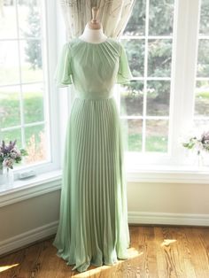 a green dress is on display in front of a window with curtains and windowsills