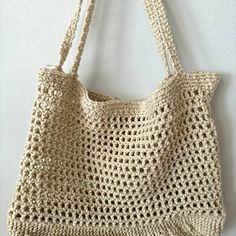 a crocheted bag hanging from a hook on a wall with the handles down