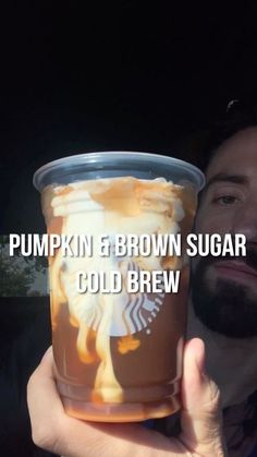 a man holding up a cup of pumpkin and brown sugar cold brew