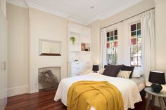 a bedroom with white walls and wood floors, along with a bed that has a yellow blanket on it