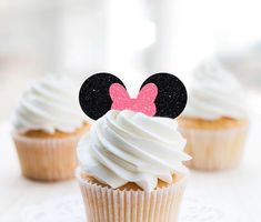 three cupcakes with white frosting and minnie mouse ears on top are sitting on a table