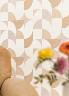 a vase with flowers in it next to a chair and wallpapered background that has geometric shapes on it