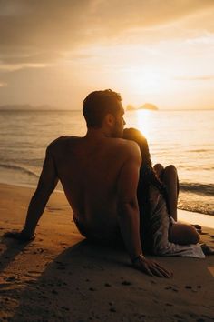 a man and woman sitting on the beach at sunset