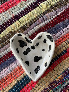 a heart shaped bowl sitting on top of a multicolored rug with black spots