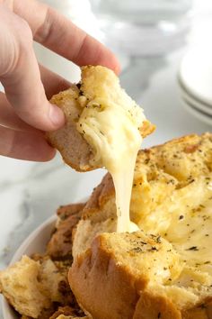 a person dipping cheese on top of bread in a white bowl with other food items