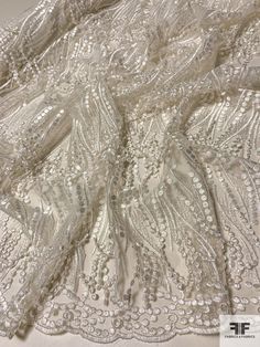 white lace fabric with beads and pearls on the bottom, as well as an openwork design