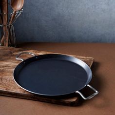 a frying pan sitting on top of a wooden cutting board next to utensils